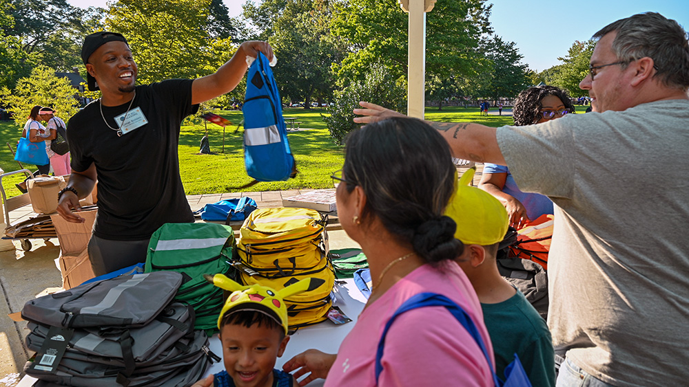 A For All Seasons associate hands a backpack to a man at an event