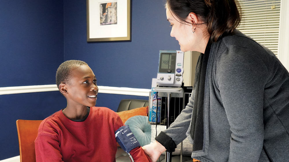 A young boy smiles up at a woman taking his blood pressure