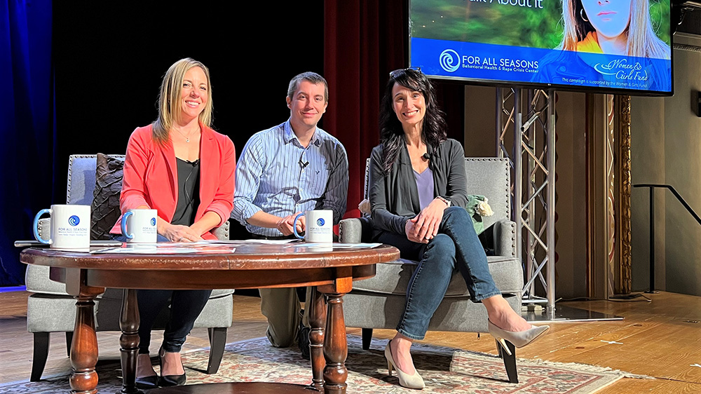 Three For All Seasons Associates on seated at a table on a stage