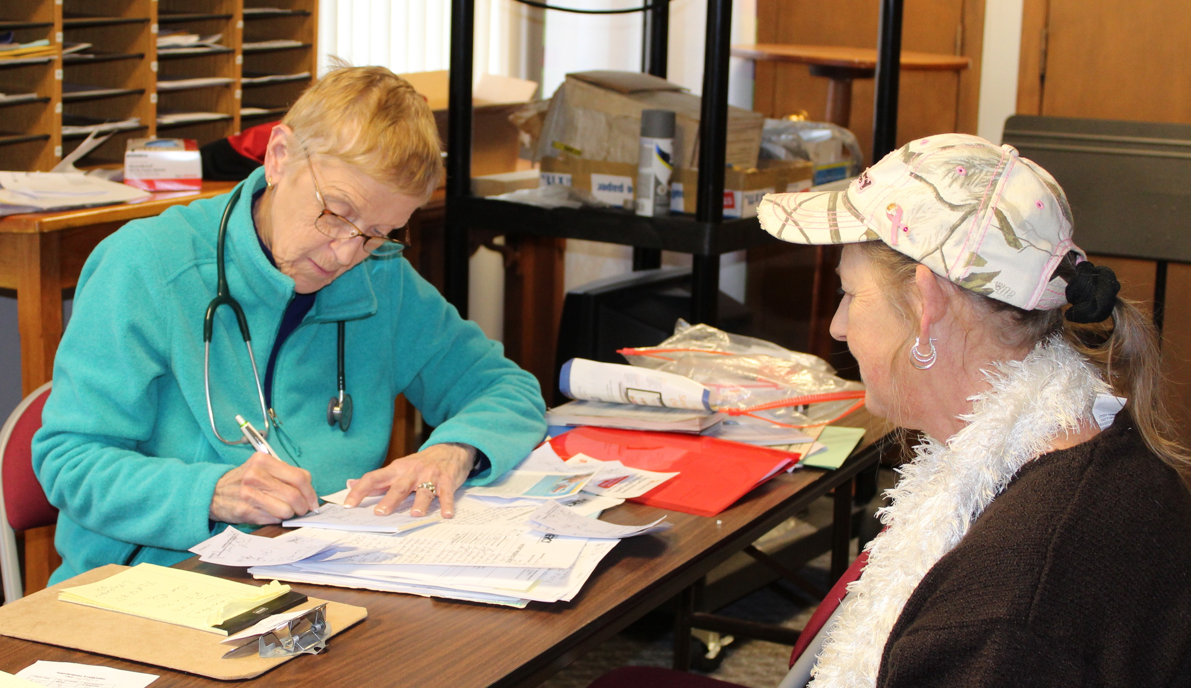 A woman filling out forms for another woman opposite her at a desk