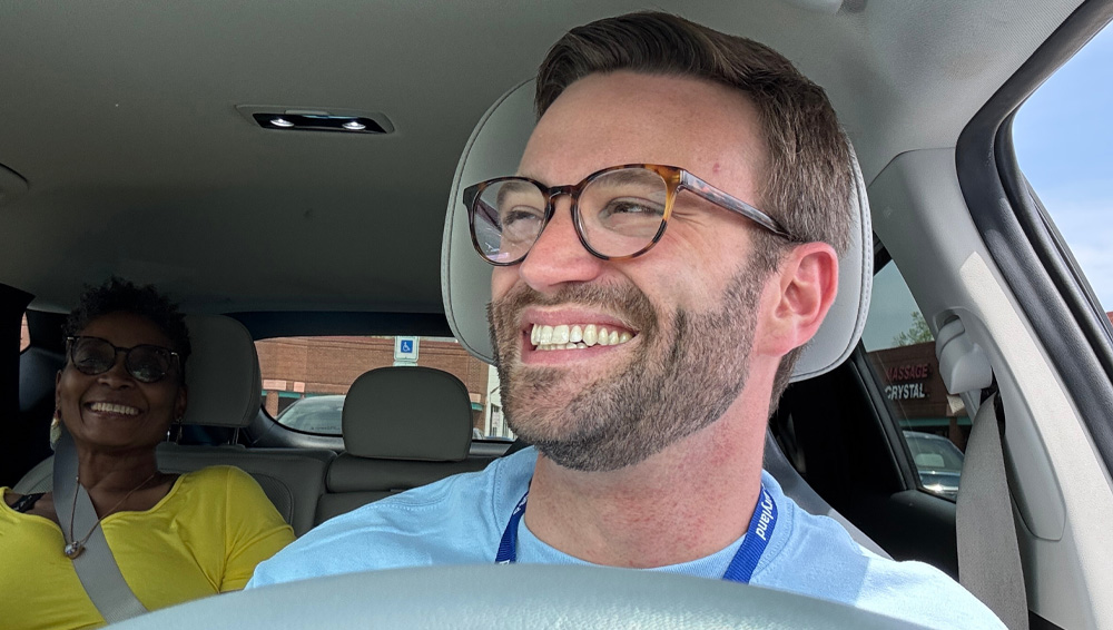 Smiling man driving a car with a rear passenger