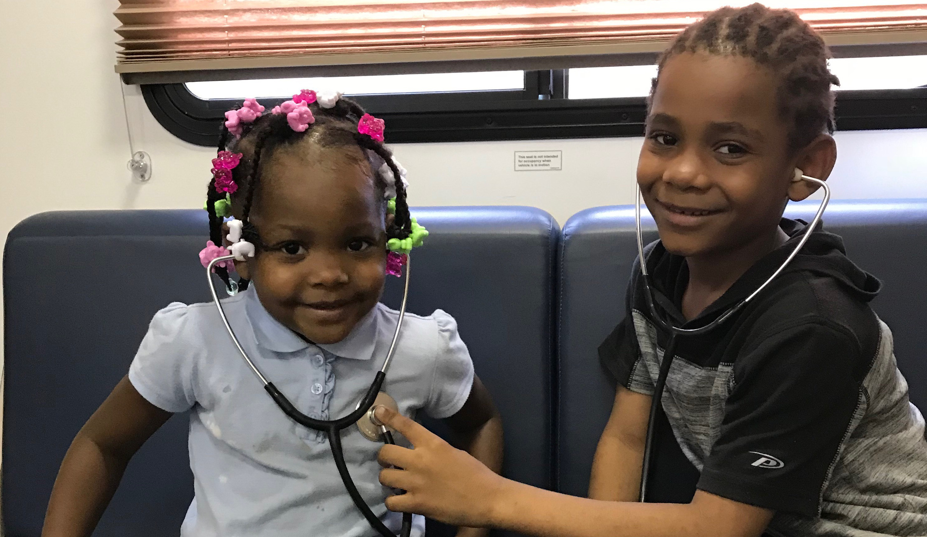 A young boy listening to the heart of a young girl with a stethoscope