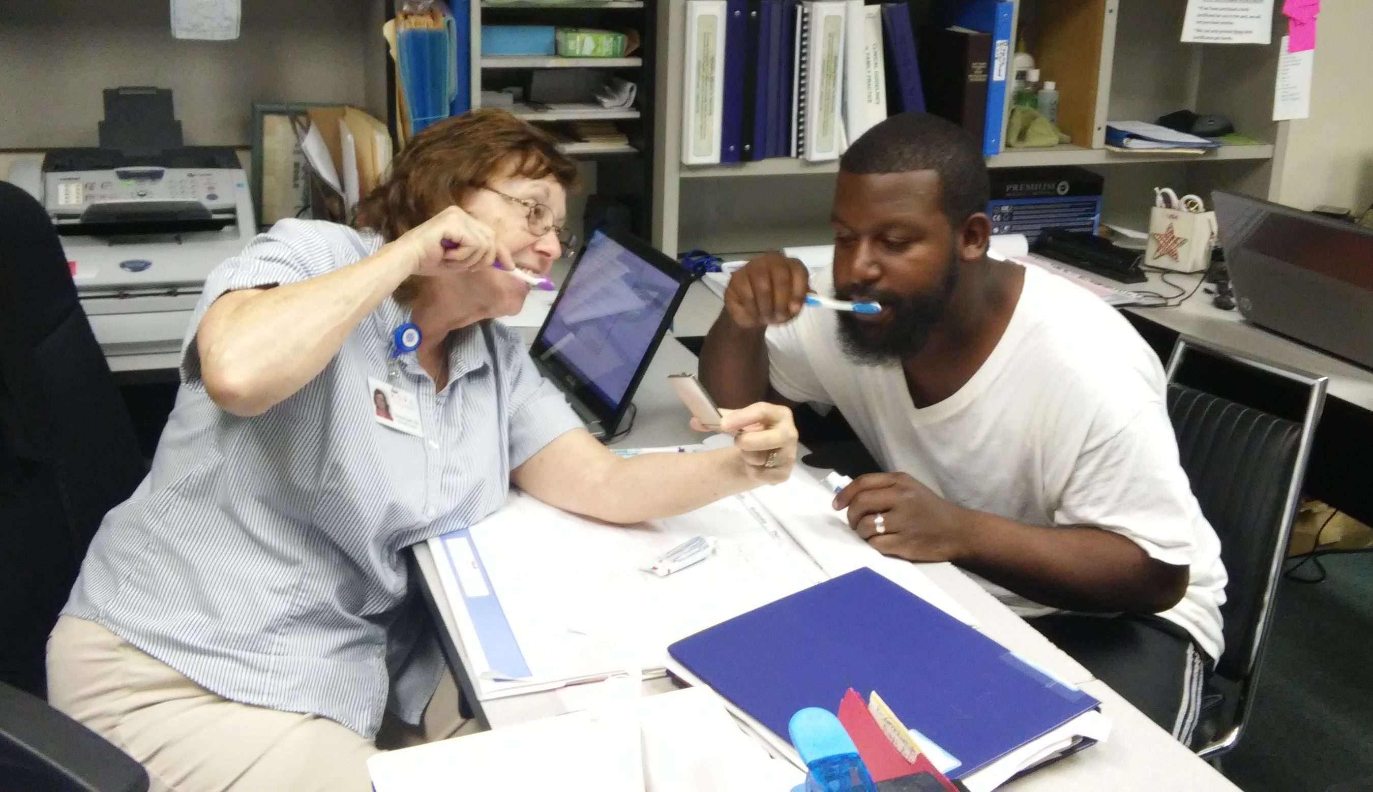 A man and woman at a desk practicing brushing their teeth