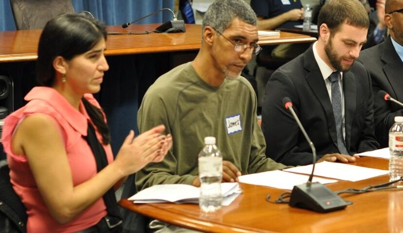 two men and one woman sitting behind a table with stick microphones extending up from the table