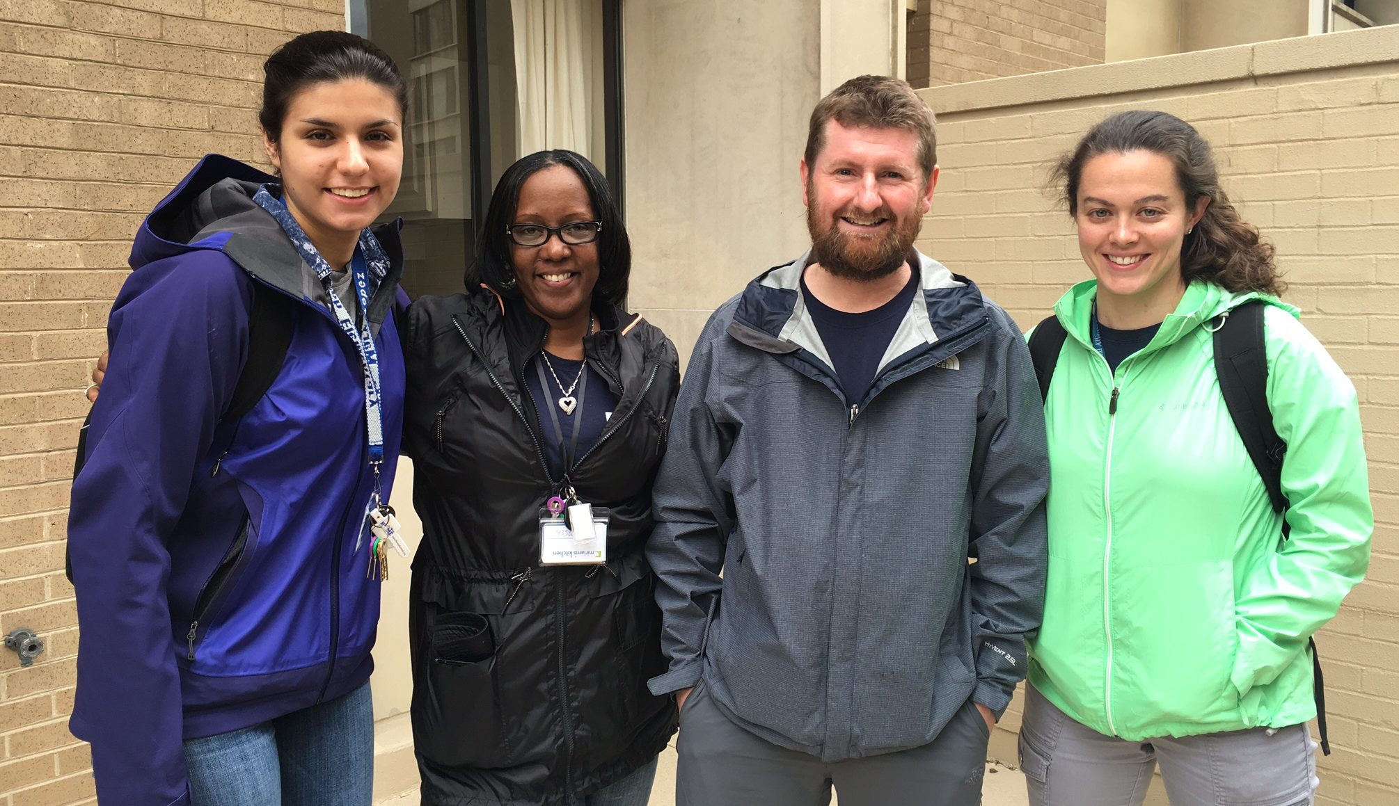 Three women and one man wearing jackets standing outside of a building facing the camera