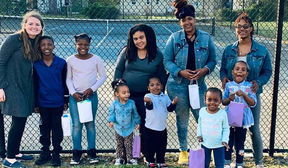 Group of mothers with children against a fence holding egg hunt baskets