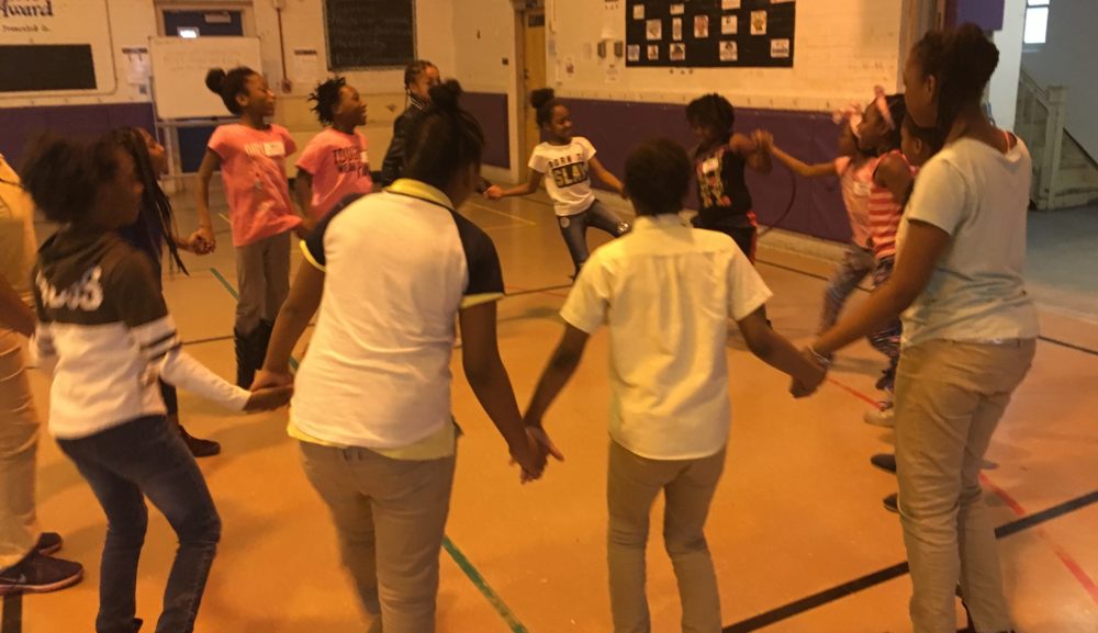 A group of girls holding hands in a circle in a gymnasium