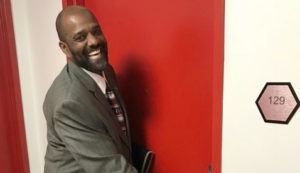 A smiling african american man in a suit opening a red door