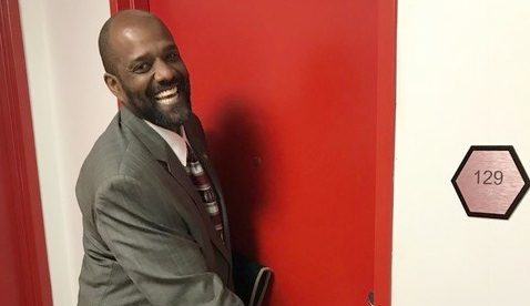 A smiling man in a suit opening a red door