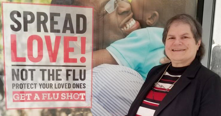 Jennifer Thomas smiling in front of a poster for flu vaccines