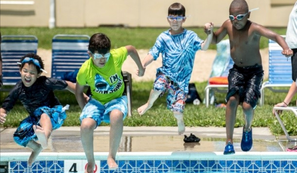 Four boys holding hands jumping into a pool together