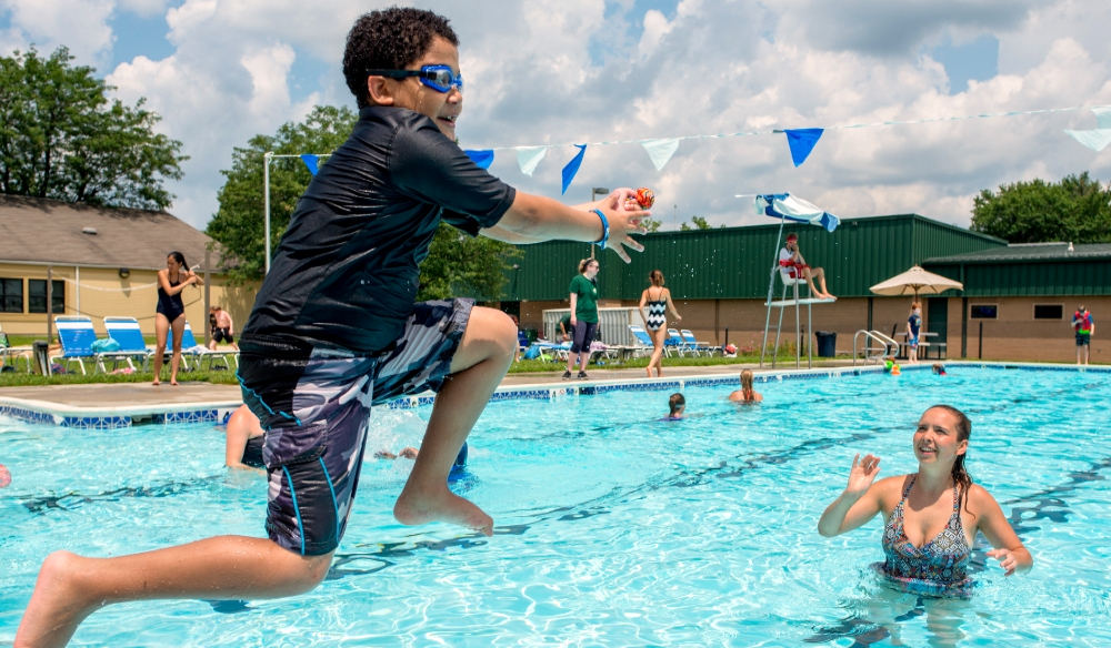 a young boy jumping into a pool catching a ball