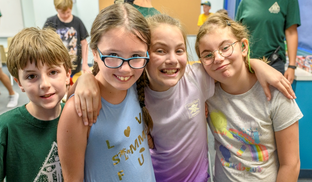 a group of four children, 3 girls with their arms around each other