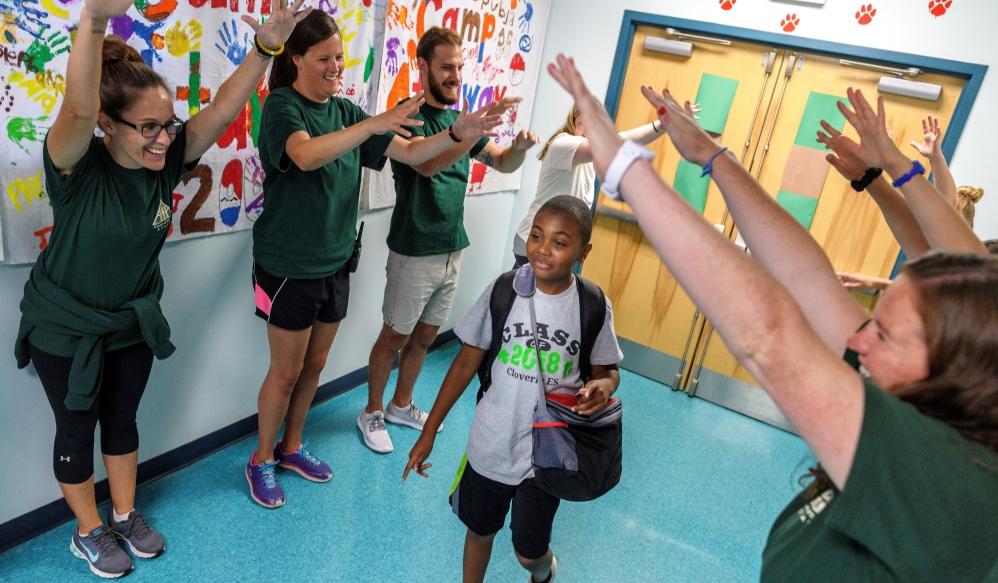 a young african-american boy walking through a group of adults who are making a tunnel with their arms