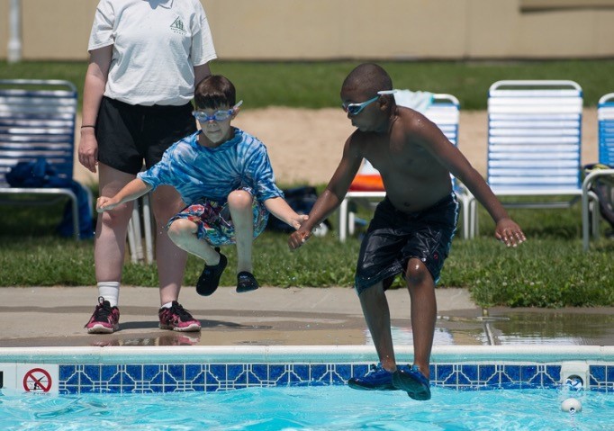 Two boys jump into a pool holding hands