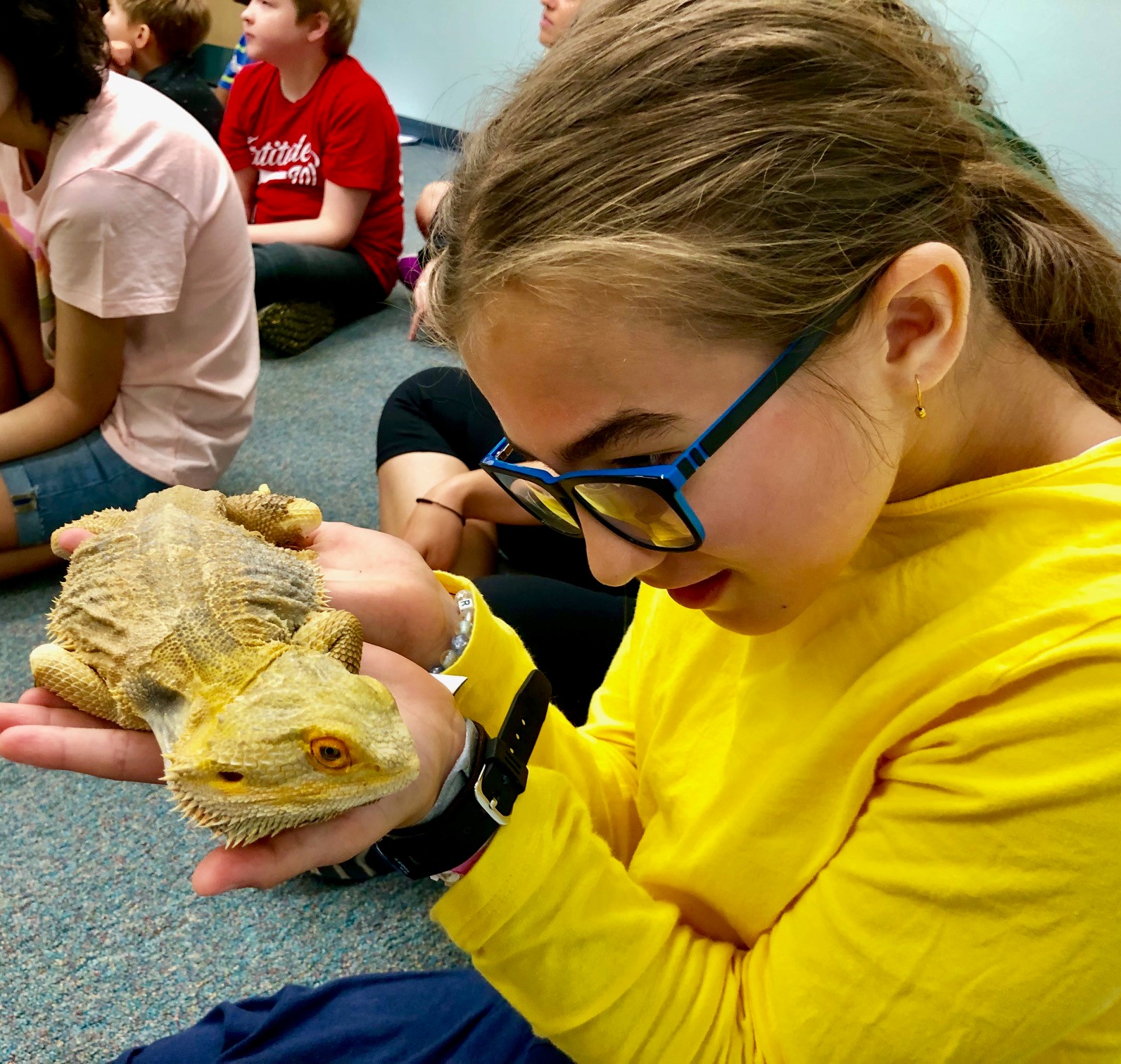 A girl with glasses holds a bearded dragon