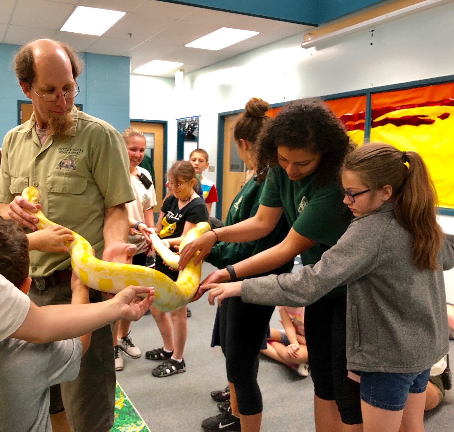 a group of girls touches a large snake held by a presenter