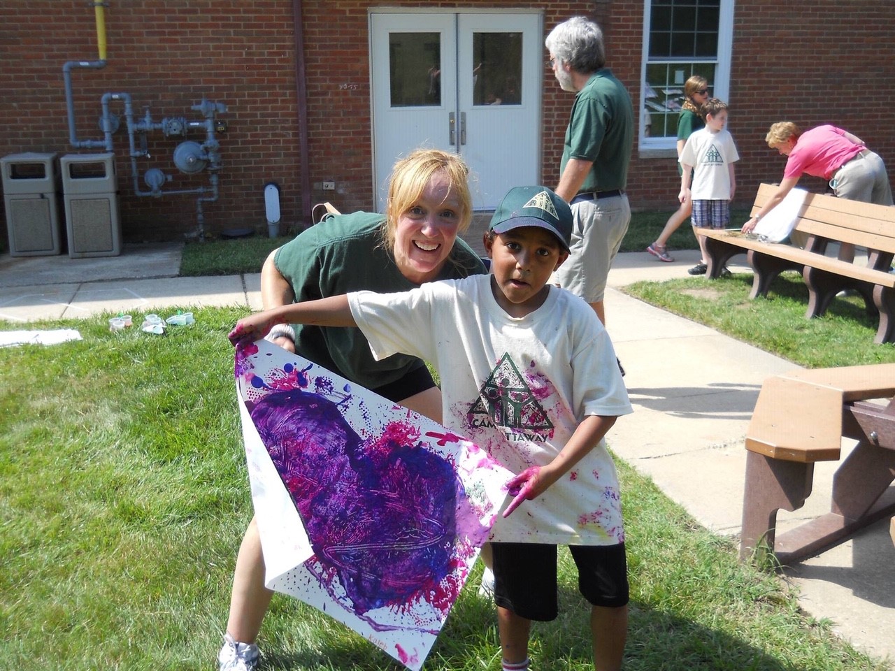 a young boy holds a painted purple heart poster posing with a camp counselor