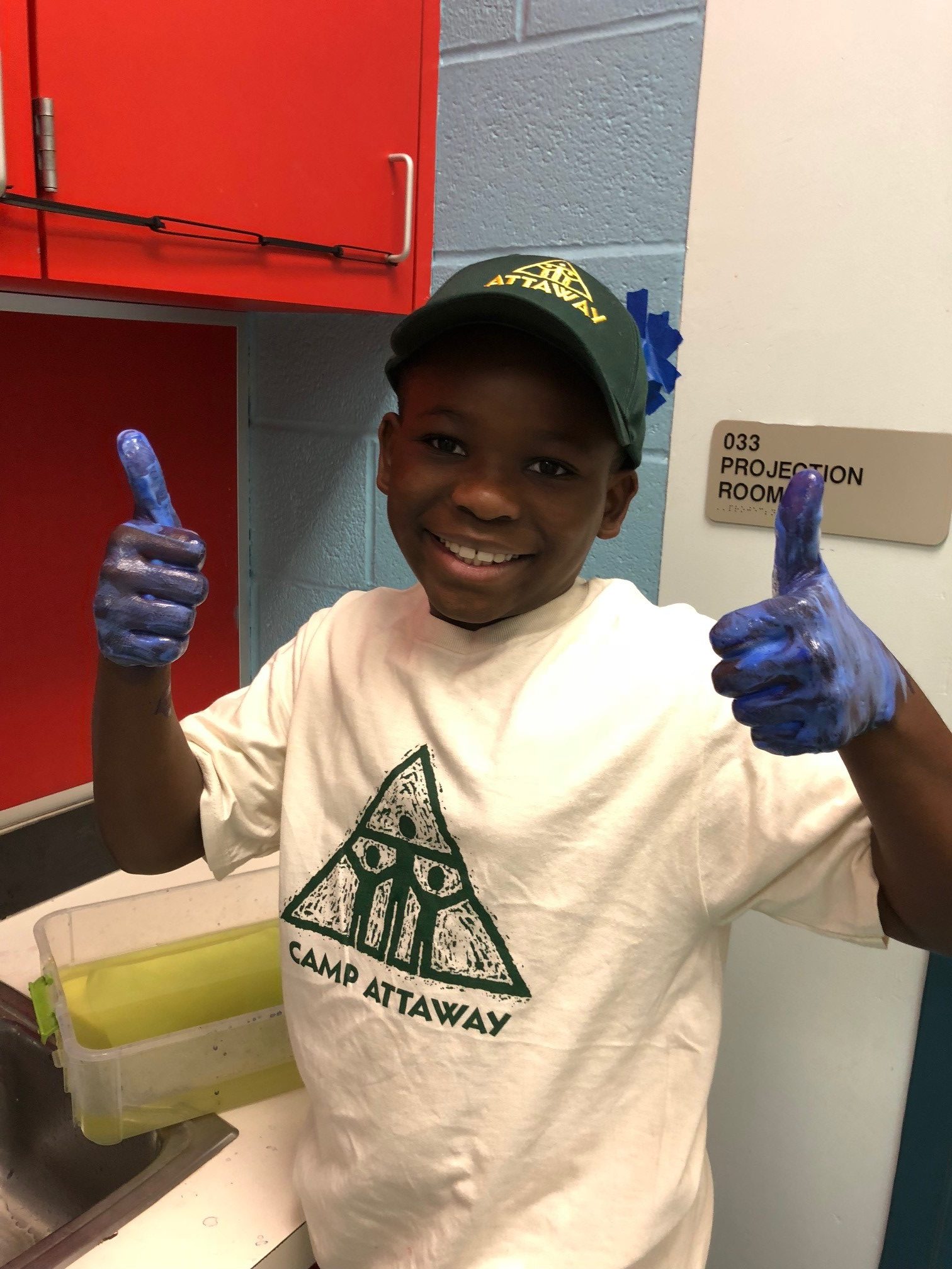 a child with blue painted hands gives double thumbs up