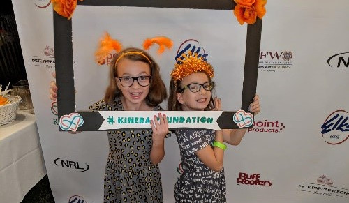 Two young girls holding a Kinera Foundation frame around their heads