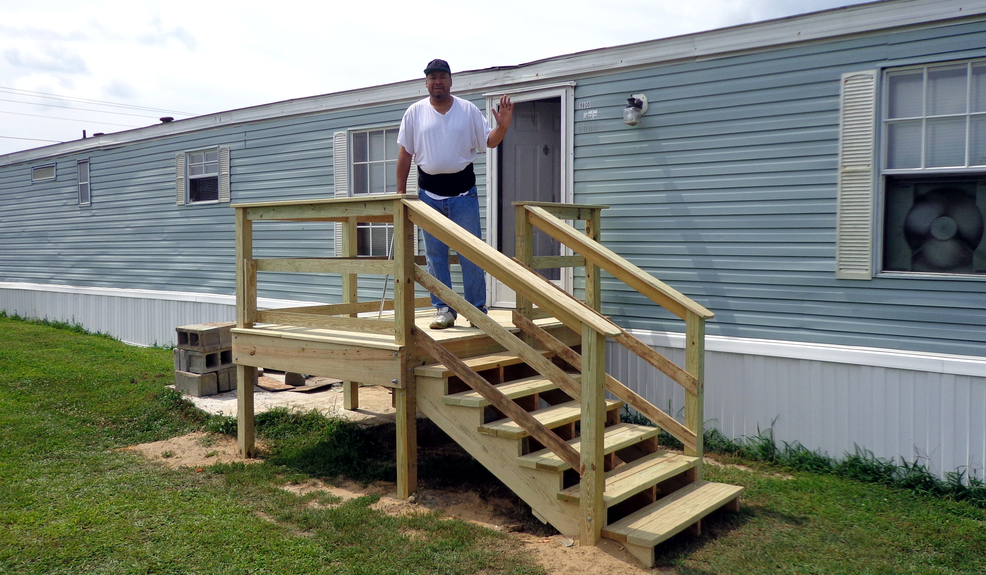 a tall man waves from his newly built porch outside of his mobile home