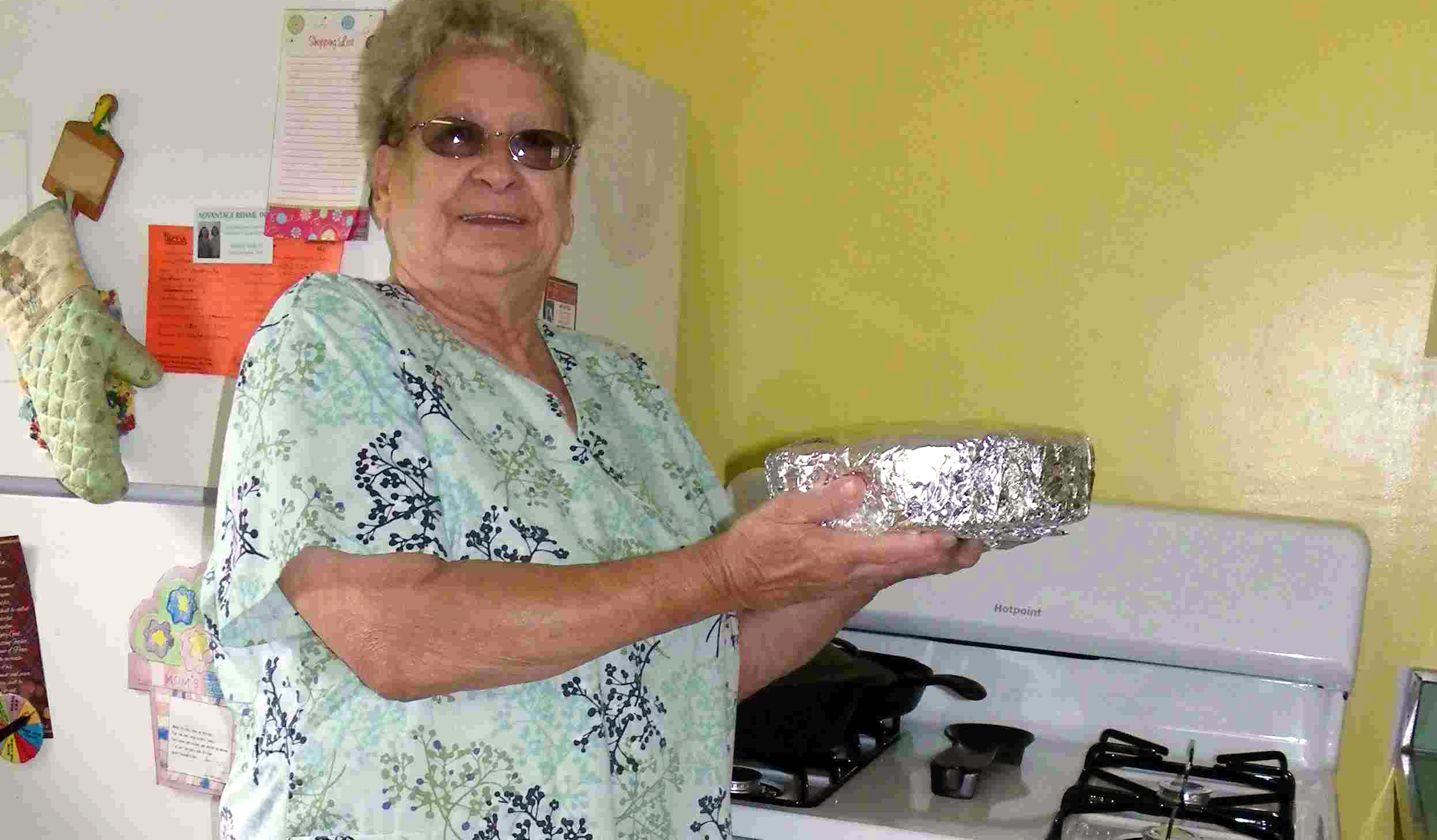 a woman holds a foil wrapped dish while standing in front of her new range