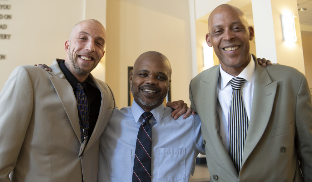 three men with arms around shoulders smiling