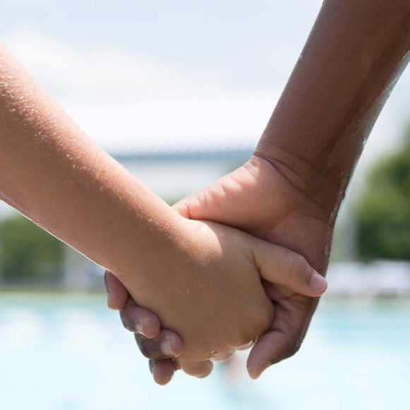 Light and dark skinned hands hold each other full frame in front of a pool