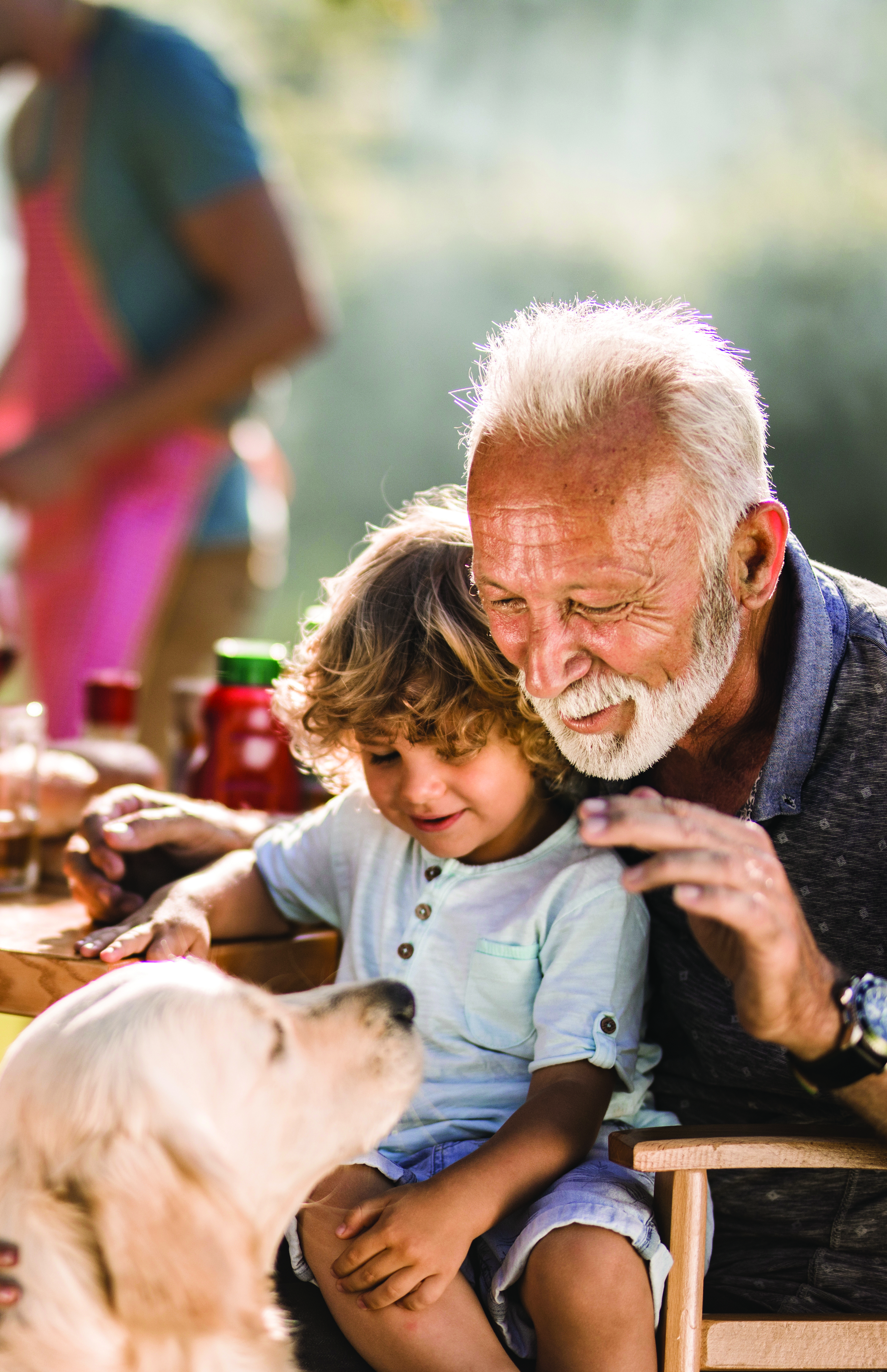 Mature man and his small grandchild enjoying on a picnic lunch with their dog.