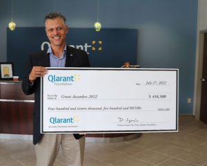 Qlarant CEO Ron Forsythe holding a huge grant check
