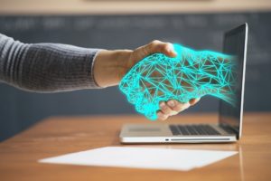 Human and digital hands shaking through a laptop monitor