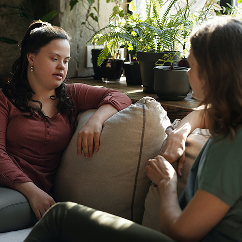 Two women, one with Down Syndrome, talk on a couch