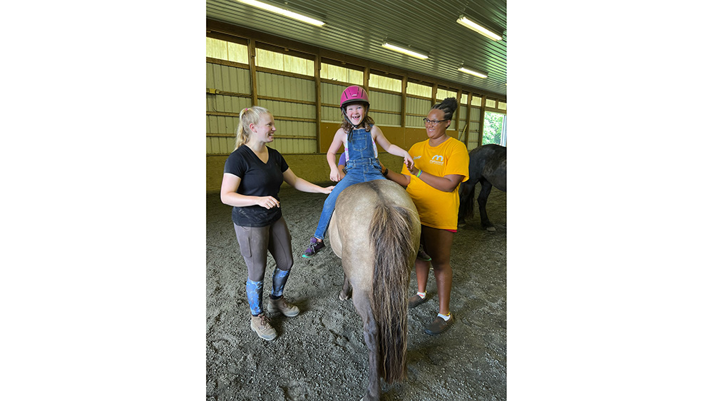 Two teenagers helping a child on a horse