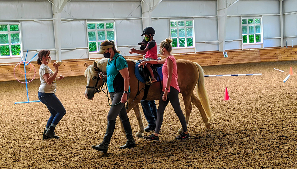 A group walking with a child on a horse indoors